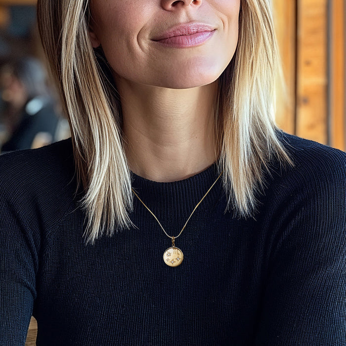 Gold zodiac charm pendant with clear diamond accents on a necklace at the neckline