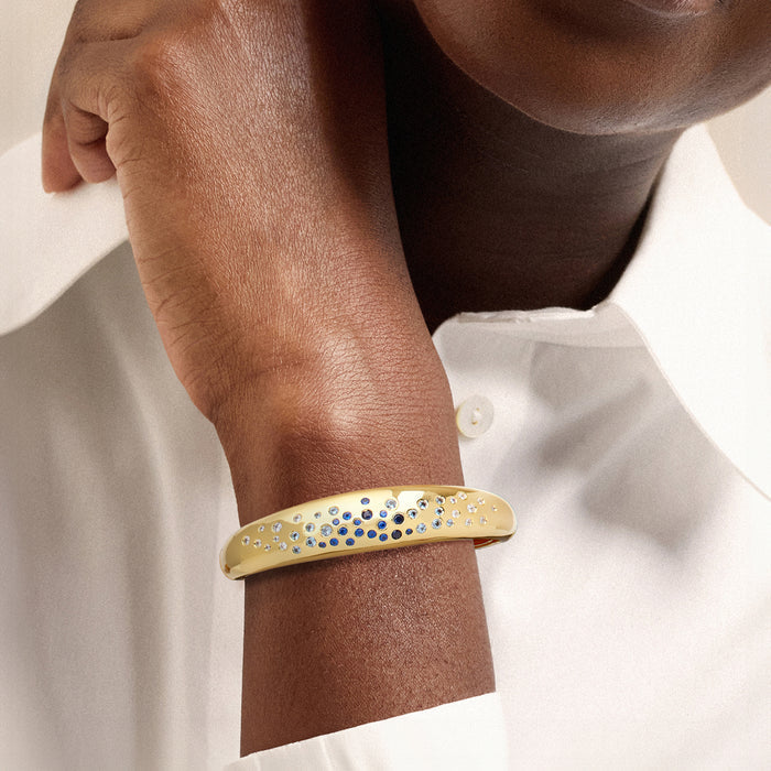 Gold-plated bangle on wrist with blue and white simulated gemstone detailing