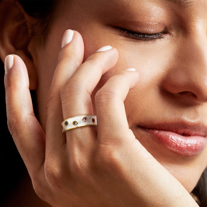 Multicolored sapphire-style ring with white enamel band worn on a finger
