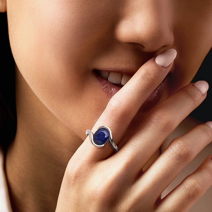 Sterling silver sapphire ring on finger with oval blue stone in curved bezel