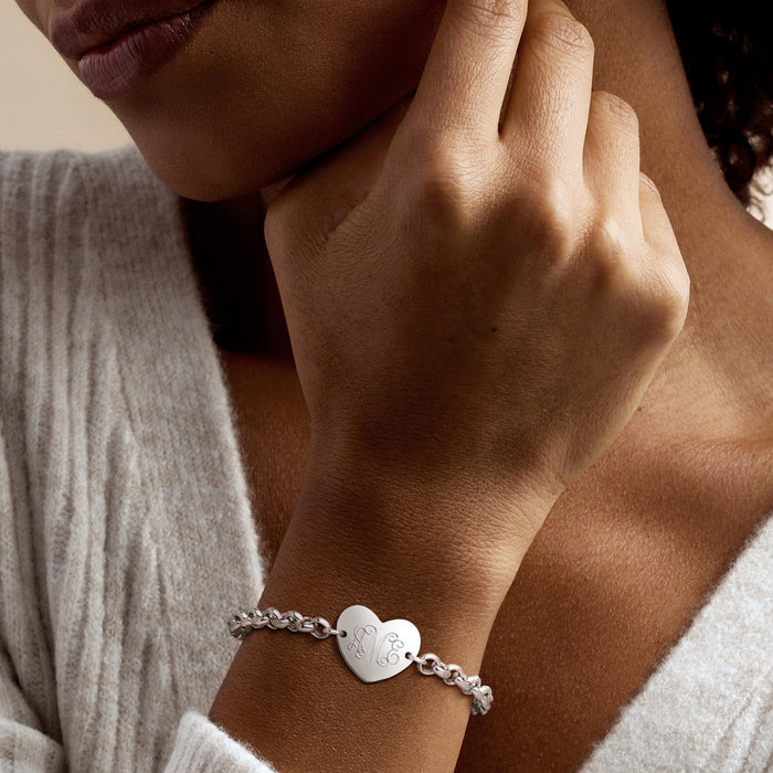 Sterling silver heart charm bracelet worn on wrist; engraved monogram heart.