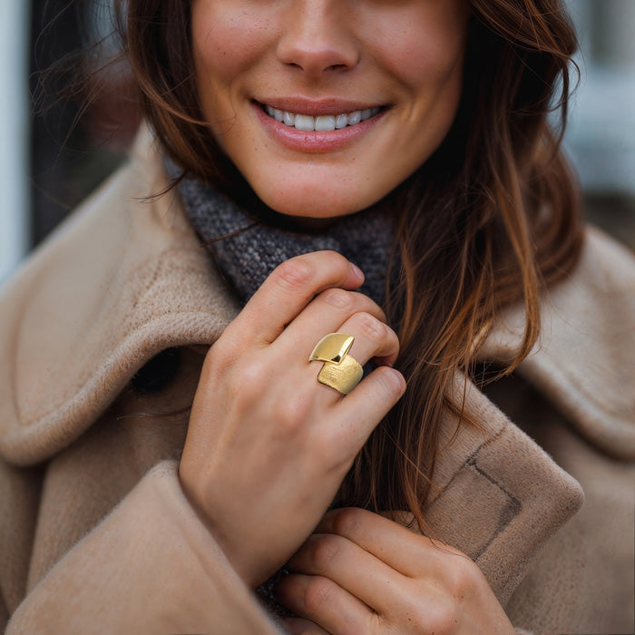 Gold-tone wrap ring worn on finger, polished square top over textured band