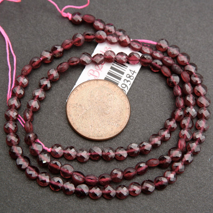 String of red beads with a coin for scale on a gray surface