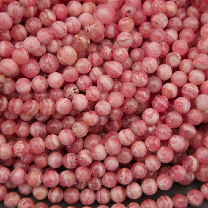 A close-up pile of round, glossy pink beads with white marbled streaks and some warm peachy-brown tones.