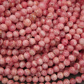 A close-up pile of round, glossy pink beads with white marbled streaks and some warm peachy-brown tones.